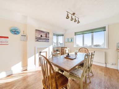 A dining room with a wooden table and chairs near windows and a wall with pictures at Bayview in Overcombe near Preston