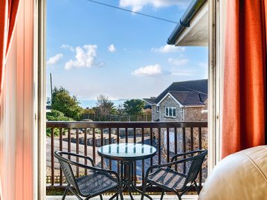 A balcony with a glass table and two black chairs overlooking a street and houses at Bayview in Overcombe near Preston