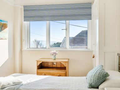 A bedroom with a window blue striped blind wooden nightstand flowers on it and a bed with a green pillow at Bayview in Overcombe near Preston