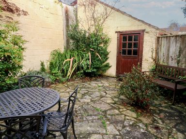 A garden with a table and chairs and a door at Bridge Cottage Budleigh Salterton