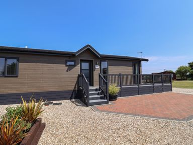 An exterior view of a single-story wooden lodge with stairs and a railing at Hazelwood 2 in Pinewood near Lyme Regis