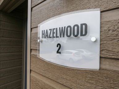 A wall-mounted sign with the text Hazelwood 2 on a wooden exterior wall at Hazelwood 2 Pinewood near Lyme Regis