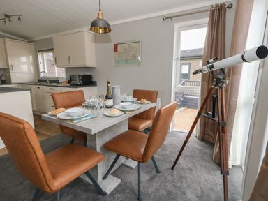 A dining area with a table set for four and a telescope by a glass door at Hazelwood 2 in Pinewood near Lyme Regis