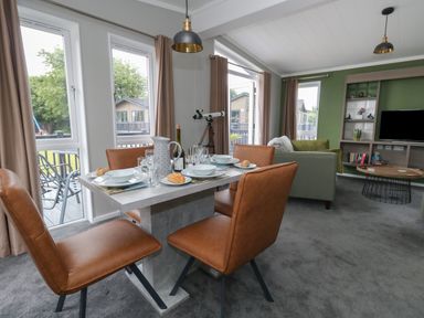 A dining table with four chairs set for a meal next to sofas and a TV in a living room at Hazelwood 2 Pinewood near Lyme Regis