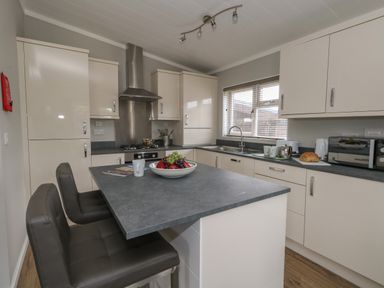 A kitchen with white cabinets a grey countertop an island with two chairs and fruit bowl at Hazelwood 2 Pinewood near Lyme Regis
