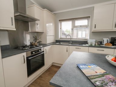 A kitchen with white cabinets grey countertops a gas stove an oven a sink under a window and a booklet on the counter at Hazelwood 2 in Pinewood near Lyme Regis