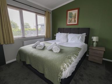A bedroom with a bed with white linens and towels on a green blanket at Hazelwood 2 Pinewood near Lyme Regis