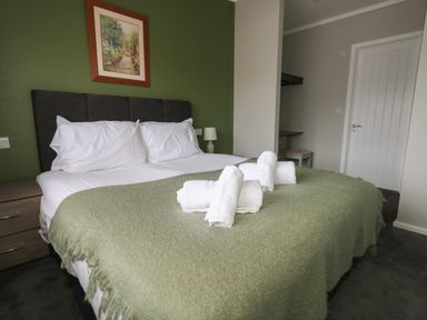 A bedroom with a double bed with white pillows and sheets a green blanket and four rolled white towels Hazelwood 2 Pinewood near Lyme Regis