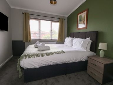 A bedroom with a large bed white linens nightstand with lamp and a window with curtains at Hazelwood 2 Pinewood near Lyme Regis