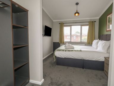 A bedroom with a bed with white linens and towels on it a wall-mounted TV and open shelving at Hazelwood 2 Pinewood near Lyme Regis