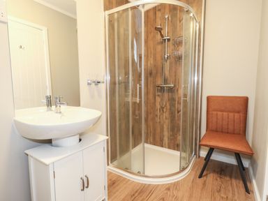 A bathroom with a corner shower with wood paneling a sink on a cabinet and a brown chair at Hazelwood 2 Pinewood near Lyme Regis
