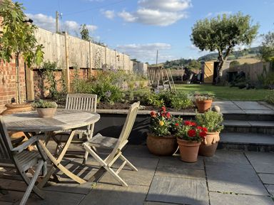 A garden with a table, chairs and flower pots at The Garden Retreat in Winchcombe