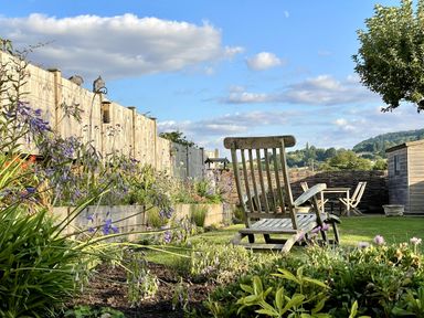 A garden with a wooden chair and table at The Garden Retreat in Winchcombe