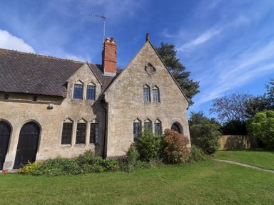 An old stone house with black windows and doors surrounded by bushes and a grassy lawn at The Alms House East in Forthampton near Tewkesbury