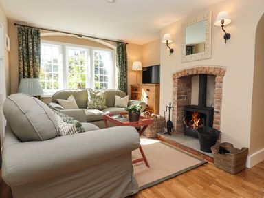 A living room with a sofa, armchair, coffee table, fireplace, wooden floor, and window at The Alms House East in Forthampton near Tewkesbury
