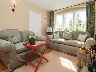 A sitting room with two sofas a small wooden table with a plant a lamp by the window and a basket of firewood at The Alms House East in Forthampton near Tewkesbury