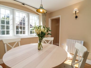 A dining area with a round wooden table and flowers in a jar on top at The Alms House East in Forthampton near Tewkesbury