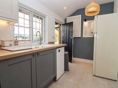A kitchen with a sink a dishwasher a refrigerator a black door and framed pictures on the wall at The Alms House East in Forthampton near Tewkesbury