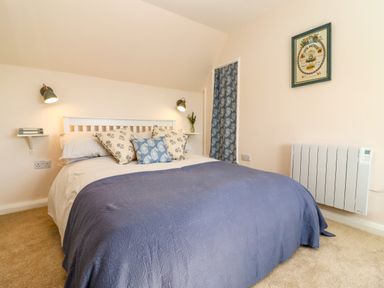 A bedroom with a bed with pillows and a blue bedspread with wall lights and a framed picture at The Alms House East in Forthampton near Tewkesbury