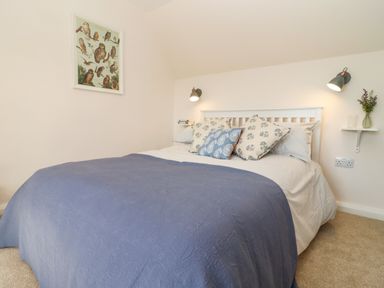 A bedroom with a double bed blue bedspread and patterned pillows two wall lamps and a framed bird print at The Alms House East in Forthampton near Tewkesbury