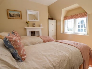 A bedroom with two beds a window a chest of drawers and a small fireplace at The Alms House East in Forthampton near Tewkesbury