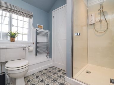 A bathroom with a toilet a shower enclosure a window with a blind a towel radiator and patterned floor tiles at The Alms House East in Forthampton near Tewkesbury