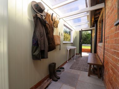 A hallway with coats and hats hanging on the wall next to rubber boots a small table and wooden bench at The Alms House East in Forthampton near Tewkesbury