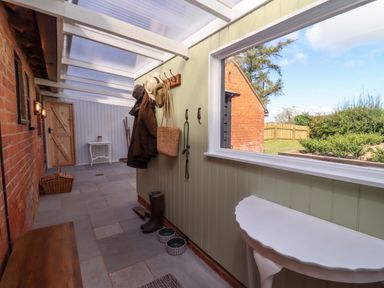 A mudroom with coats hanging on hooks boots and pet bowls on the floor and a window looking outside at The Alms House East in Forthampton near Tewkesbury