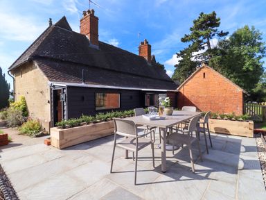 An outdoor patio area with a table and four chairs beside a house with brick and black siding at The Alms House East in Forthampton near Tewkesbury