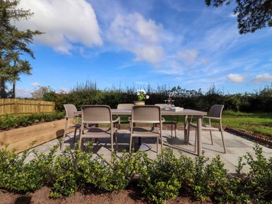An outdoor patio with a table and six chairs surrounded by greenery at The Alms House East in Forthampton near Tewkesbury