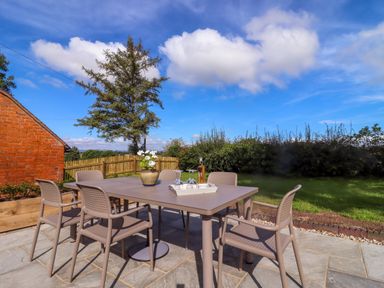 An outdoor patio area with a table and six chairs on stone flooring at The Alms House East in Forthampton near Tewkesbury