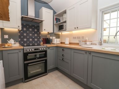 A kitchen with grey and white cabinets a stove and oven a microwave toaster and kettle at The Alms House East in Forthampton near Tewkesbury