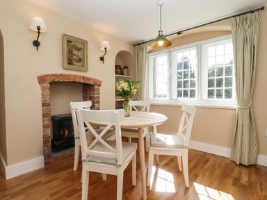 A dining area with a round table and four chairs near a window with curtains and a brick fireplace at The Alms House East in Forthampton near Tewkesbury