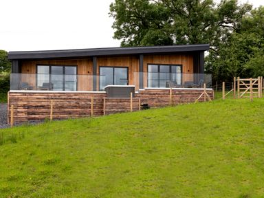 A modern wooden house with glass balcony railings and outdoor seating on a grassy hillside at The Lookout in Longridge