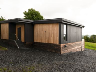 A modern house with mixed dark and light wood paneling and a glass railing near the door at The Lookout in Longridge