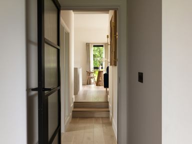 A hallway with wooden flooring leading to a room with a wooden chair a round wooden table a vase with flowers and a window at The Lookout in Longridge