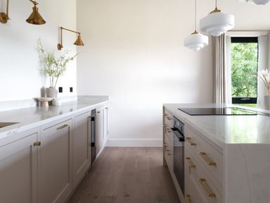 A kitchen with white cabinets and gold handles marble countertops and two pendant lights by a window at The Lookout in Longridge
