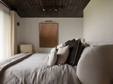 A bedroom with a large bed with multiple pillows a beige armchair and a wall painting at The Lookout in Longridge