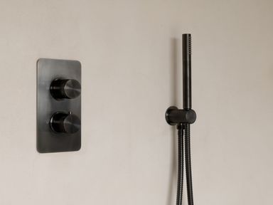 A black wall-mounted shower control panel with two knobs and a handheld showerhead attached to the wall at The Lookout in Longridge