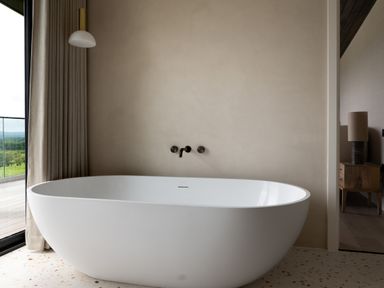 A white freestanding bathtub with wall-mounted faucet and a curtain beside a glass door overlooking greenery at The Lookout in Longridge