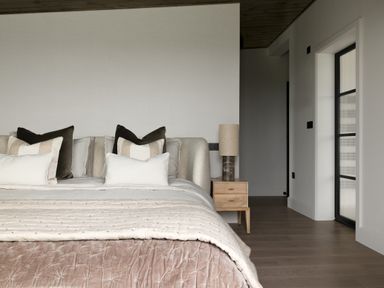 A bedroom with a bed with multiple pillows a wooden nightstand with a lamp and a door on the right at The Lookout in Longridge