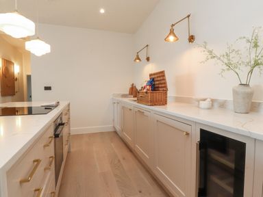 A kitchen with white countertops brass handles a wine cooler hanging lights and a vase with branches at The Lookout in Longridge