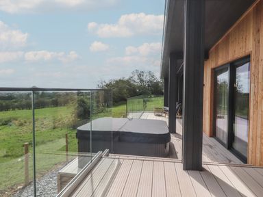 A wooden deck with glass railing a covered hot tub outdoor chairs and table at The Lookout in Longridge