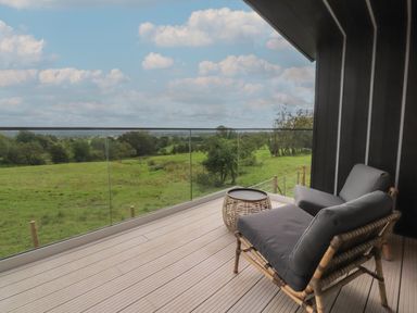 A balcony with a cushioned chair and small table overlooking a green field at The Lookout in Longridge