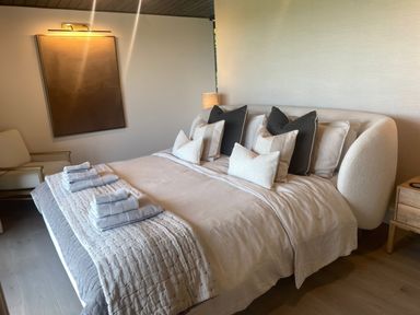 A bedroom with a large bed with folded towels and pillows a chair a nightstand and a wall light at The Lookout in Longridge