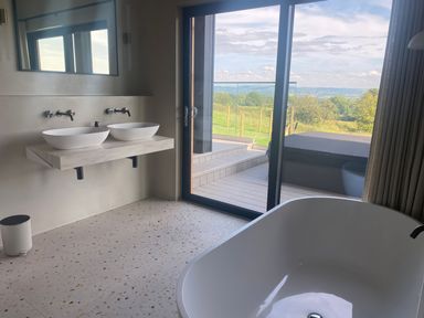 A bathroom with two sinks a freestanding bathtub and a glass door leading to a deck with a hot tub and a view of greenery at The Lookout in Longridge