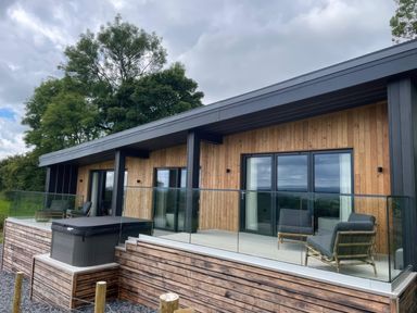 A wooden exterior balcony with glass railings lounge chairs and a hot tub at The Lookout in Longridge