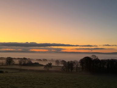 A rural landscape with trees and a building under a misty sky at sunrise at The Lookout in Longridge