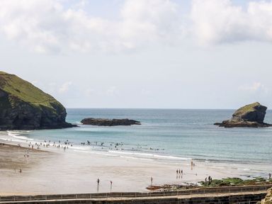 A beach with people walking and swimming near rocky cliffs and outcrops at Bay View in Portreath