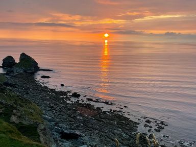 A rocky coastline with the sun setting over the sea at Bay View in Portreath